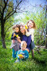 Naklejka na ściany i meble Mom with three children - a boy and two girls smiling, and her children are hugging. Happy large family in nature.