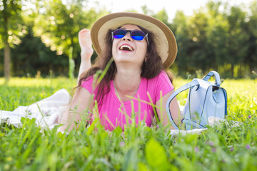 portrait of happy young woman with hat and sunglasses lying in park on picnic