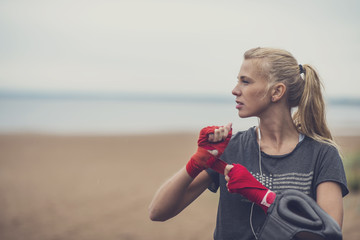 Young sporty blonde woman standing in a boxing stance wrapping her wrists before the boxing training
