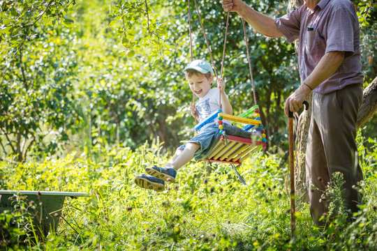 Senior Man Pushing Cheerful Grandson On Swing