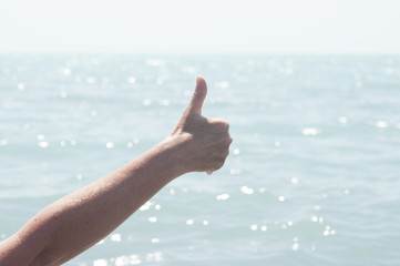 The hand with the gesture on the background of blue sea.