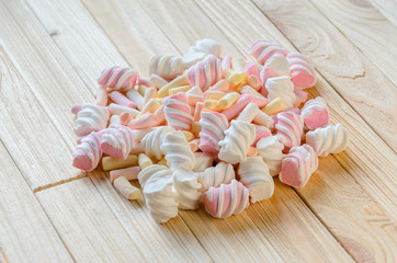 Multicolored marshmallows on bright wooden table. Background of multi-colored and different in shape and size of marshmallows. Sweets background