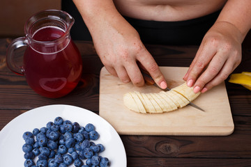 Overweight fat woman slicing a banana for fruit plate. Juicy tasty low-calorie dessert for weight losing, dieting, healthy food concept
