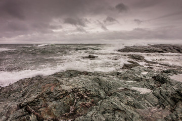 Waves break against the rocky coastline in Newport, Rhode Island, under a stormy sky