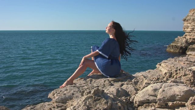 The girl in the blue dress sitting by the sea. A strong wind