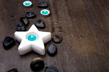 Turquoise candles in white star candle holder on gray slate background with water droplets