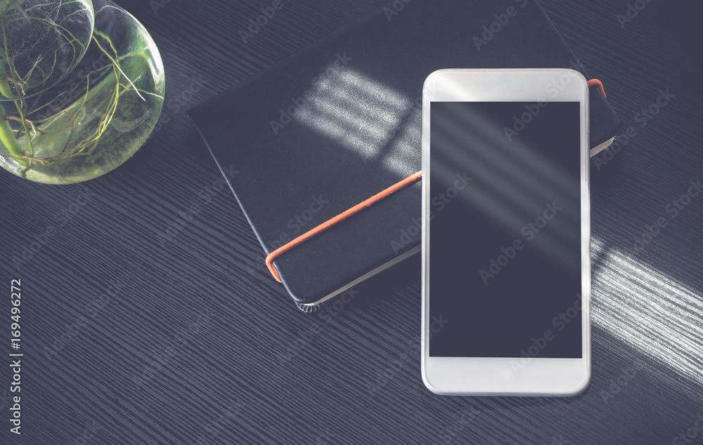 Fototapete blank screen of mobile phone lay on notebook near window with plant in pot on black wooden modern de