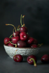 Cherry in a  ceramic cup On a black worn background. Dark key. Harvest of sweet cherry