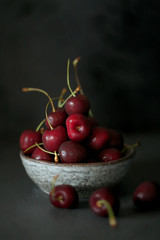 Cherry in a gray ceramic cup On a black worn background. Dark key. Harvest of sweet cherry