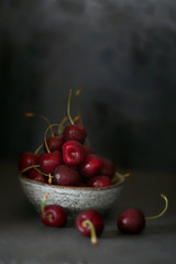 Cherry in a gray round ceramic cup On a black worn background. Dark key. Harvest of sweet cherry