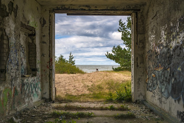 Coastal landscape with dune, Baltic Sea and pine trees seeing through a frame of old destroyed building