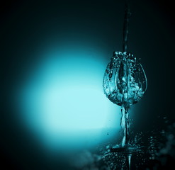 Motion of pouring splash water in transparent wine glass with reflect of light backdrop.