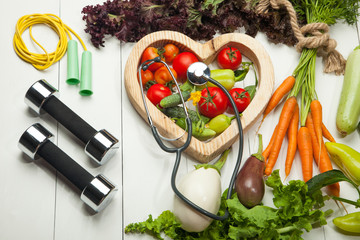 Fresh vegetables, dumbbells and heart on a white background