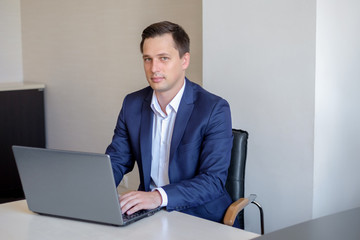 businessman is working with laptop in office is looking at the camera.