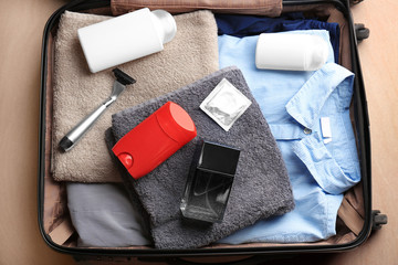 Suitcase with clothes, towels and different male hygiene items on floor