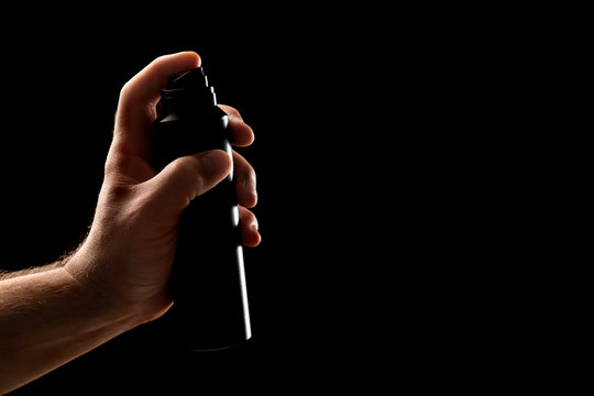 Hand Of Man Holding Deodorant On Dark Background