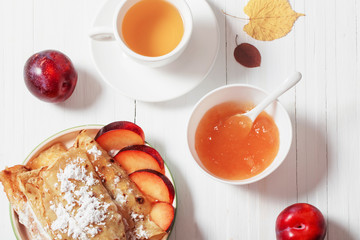 pancakes with tea  and plums on white wooden table