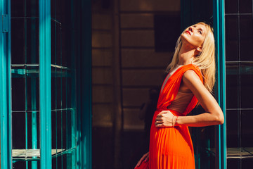 Portrait of young beautiful tanned blonde woman in ogange evening dress posing outdoor in hot summer day.