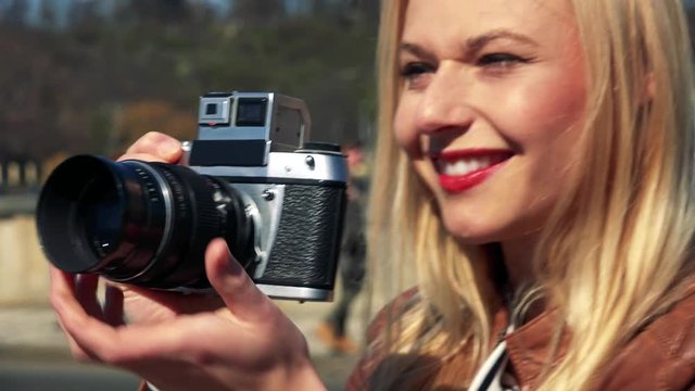 A young attractive woman takes photos with a camera in a street in an urban area - face closeup