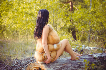 Luxurious naked lady in fur coat made of fox fur in the forest. Attractive slender brunette with red lips in furs. Sexy European woman attracts men