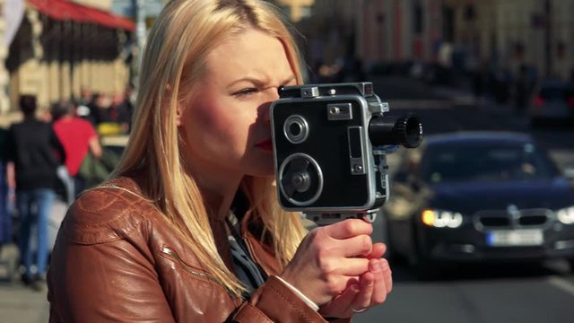 A young attractive woman shoots a video with a camera - closeup - a busy street in the blurry background