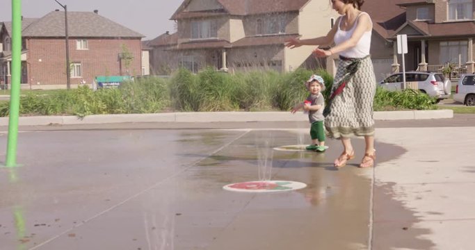 Mother Running Through Sprinklers With Toddler Son - Slow Motion