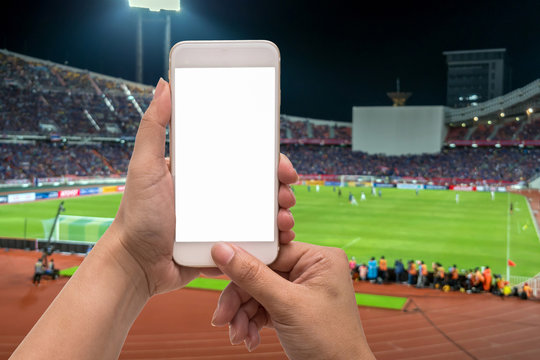 Female hand holding mobile smart phone touch screen on blurred of action photographer taking photo at player in Abstract blurred photo of soccer stadium, sport background concept