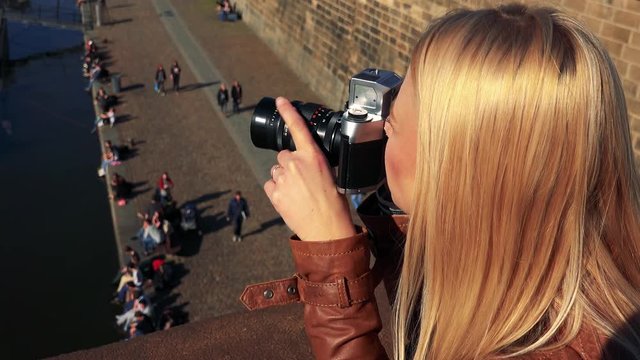 A young attractive woman takes photos with a camera from a bridge - closeup - a river and people on a shore in the blurry background