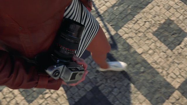 A woman holds a camera and walks down a street - closeup from above on the hand