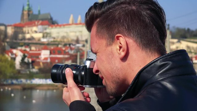 A young handsome man takes photos with a camera - face closeup from the side - a townscape in the blurry background