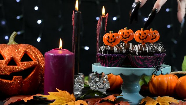 Halloween party table with spooky hand with long black nails stealing a chocolate cupcake.