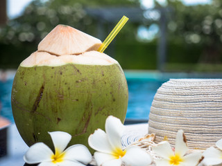 Young coconut or coconut water put on table with hat beside swimming pool.