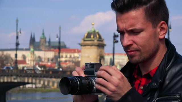 A young handsome man takes photos with a camera - face closeup - a quaint town in the blurry background