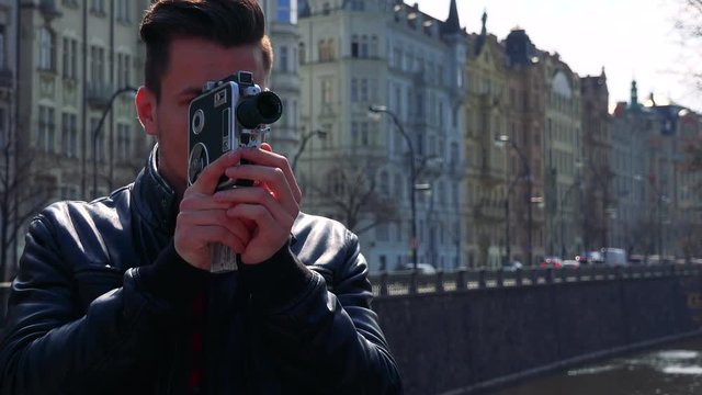A young handsome man shoots a video with a camera - closeup - buildings of a quaint town in the blurry background