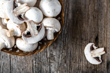 Fresh champignon mushrooms in a basket on wooden table, overhead