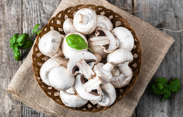 Fototapeta premium Fresh champignon mushrooms in a basket on wooden table, overhead