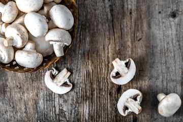 Fresh champignon mushrooms in a basket on wooden table, overhead