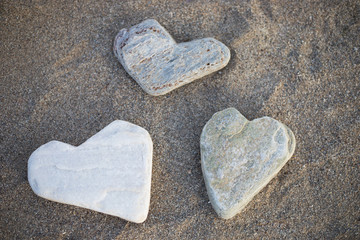 Three stones shaped in a form of hearts are on the beach by the sea. Holiday mood collection of people for good luck, happiness, love, to remember good moments of the travel to an interesting place.