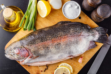 Trout spent raw on a cutting wooden board with spices, herbs, salt, lemon and olive oil. Top view