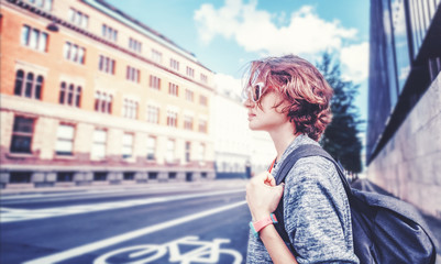 young beautiful woman with a short haircut and a backpack stands on the background of a road and buildings in the city