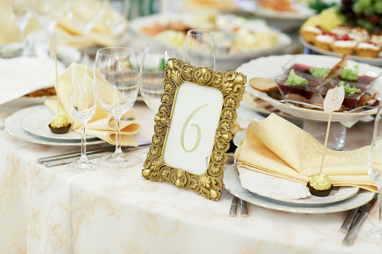 Number 6 put in a golden frame stands among white plates on dinner table