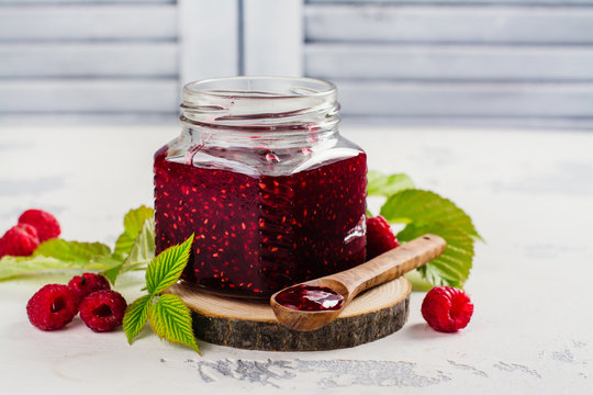 Raspberry jam in a glass jar and fresh raspberry on white stone table