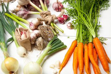 Fresh vegetables, garlic, onions and carrots on a white wooden table. View from above.
