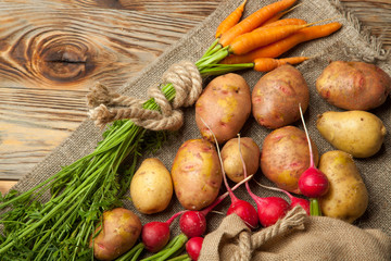 Potatoes, radishes and carrots on a rustic wooden background