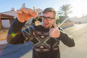 Young smiling man showing keys to new home. Real estate, apartment and people concept