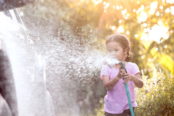 Naklejka premium Happy asian child girl help parent washing car on water splashing with sunlight