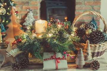 Cosy Christmas composition, presents and decorations on the table in front of the fireplace with woodburner, lit up Christmas tree with baubles and ornaments and garlands, selective focus, toned