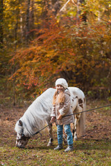 Little cute girl walking with a pony in the autumn forest