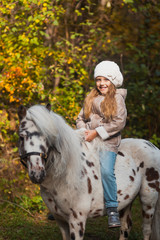 Little beautiful girl sitting on a pony in the autumn park