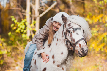 Little beautiful girl sitting on a pony in the autumn park